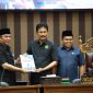 Plt Asisten Pemerintahan dan Kesra, Wisnu Wardhana (kiri), menyerahkan dokumen Raperda Pembentukan Desa Baru kepada Ketua Bapemperda DPRD Tanah Bumbu, H. Harmanudin (tengah), disaksikan oleh Wakil Ketua I DPRD Tanah Bumbu, H. Hasanuddin (kanan), dalam Rapat Paripurna DPRD Tanah Bumbu, Senin (6/10/2025).